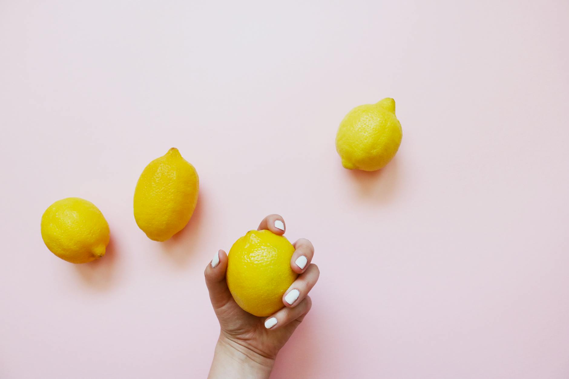 A hand holding a bright lemon on soft pink background, symbolizing gentle touch and recovery