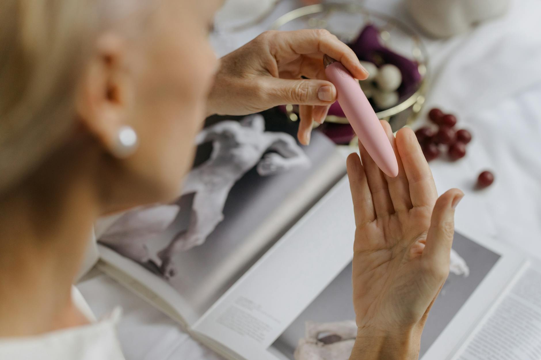 A hand holding a pink vibrator against art books in the background