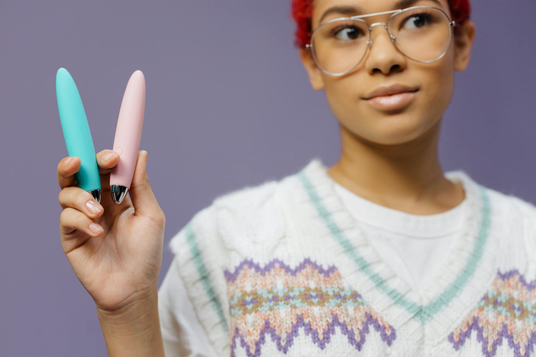 Hands holding colorful vibrators against a purple background, representing choice and agency in pleasure